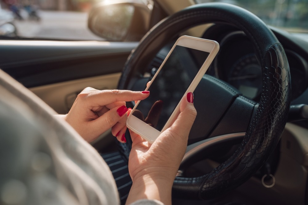 Conductora de Uber distra&iacute;da usando su tel&eacute;fono mientras maneja en West Palm Beach representando el comportamiento negligente que causa accidentes de Uber y da lugar a reclamaciones legales
